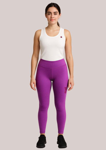 Woman wearing a white tank top and purple leggings on a light gray background